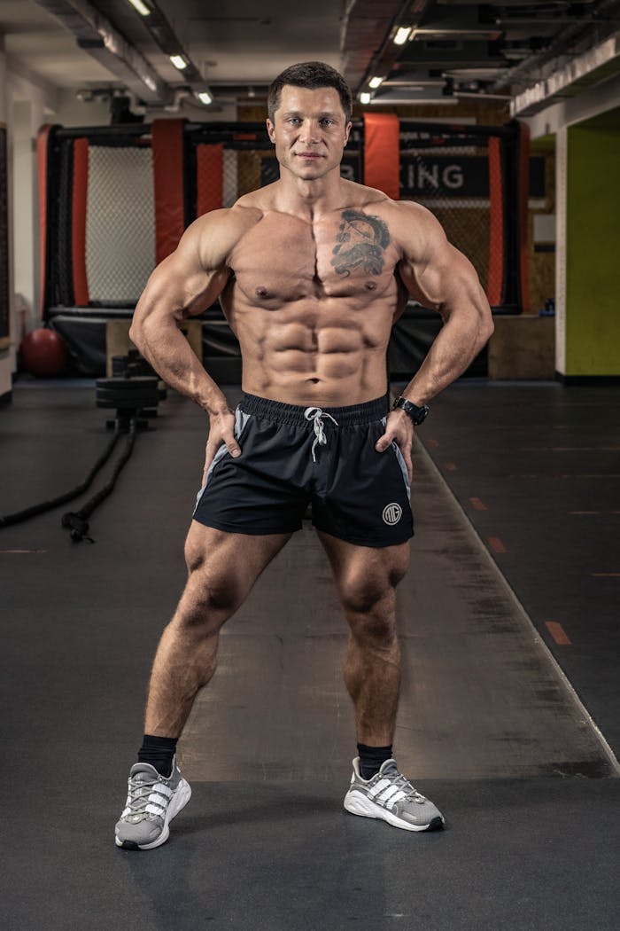 Muscular man with tattoos posing confidently in an indoor gym.